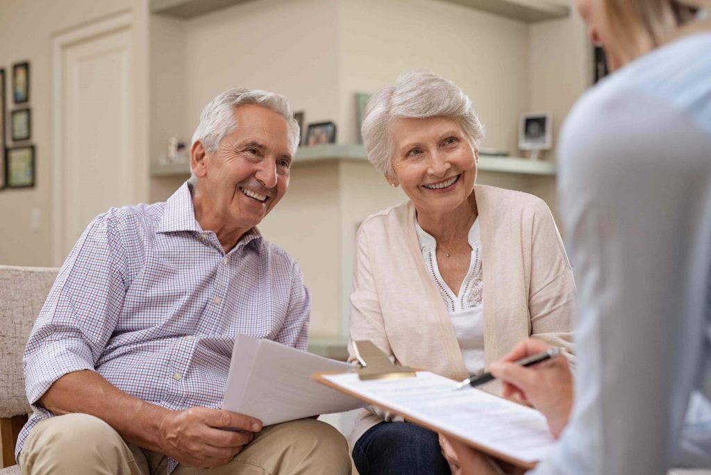 Elderly couple smiling at lawyer out of frame holding paperwork.